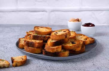 Rusks with dried cranberries and pistachios on a ceramic plate on a light background