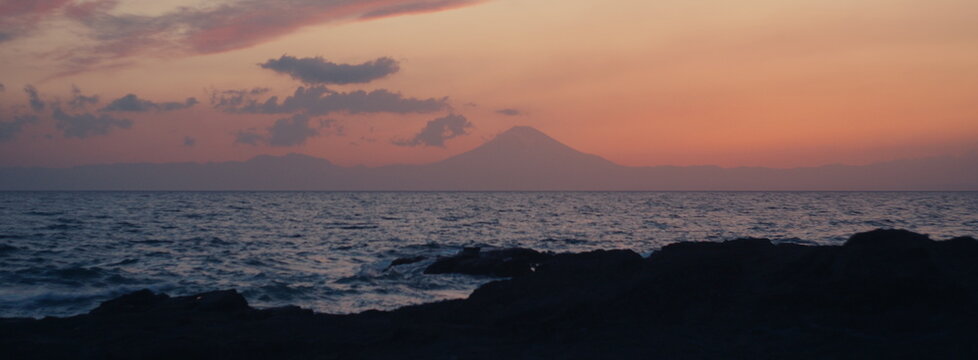 Distant Mount Fuji glowing in soft sunset haze above the sea.