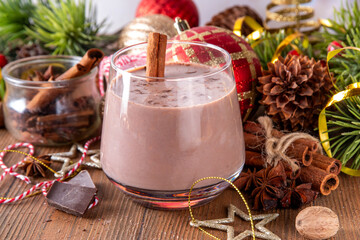 Spiced chocolate eggnog punch cocktail, served with cinnamon stick, sprinkle of nutmeg and chocolate, on cozy Christmas background 