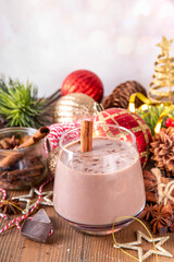Spiced chocolate eggnog punch cocktail, served with cinnamon stick, sprinkle of nutmeg and chocolate, on cozy Christmas background 