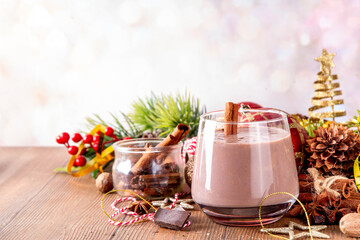 Spiced chocolate eggnog punch cocktail, served with cinnamon stick, sprinkle of nutmeg and chocolate, on cozy Christmas background 