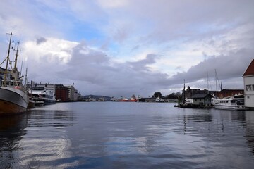 Scenic view of Bergen harbor in Norway featuring colorful historic buildings of Bryggen, boats docked in the calm water, and a cloudy sky.