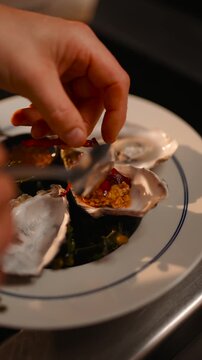 A person is putting a red string on a plate of oysters. The plate is white and has a blue border