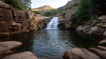 A beautiful waterfall cascades into a dark pool framed by rugged rock formations in a serene mountain landscape