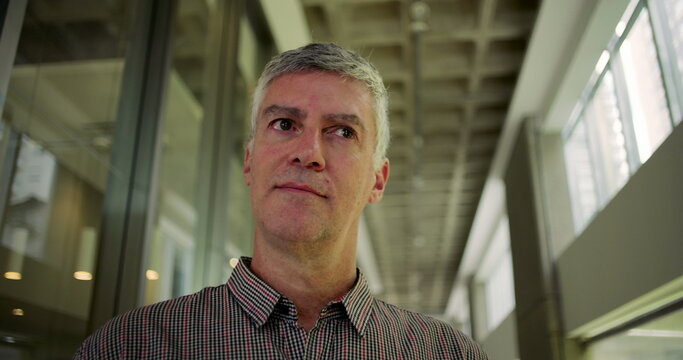 Middle aged man looking away with pensive expression in modern office hallway thoughtful moment of contemplation leadership maturity and introspection - Powered by Adobe