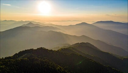 Aerial view of a mountain range at sunset, with layers of hills and a hazy atmosphere, illuminated by the sun's golden light.