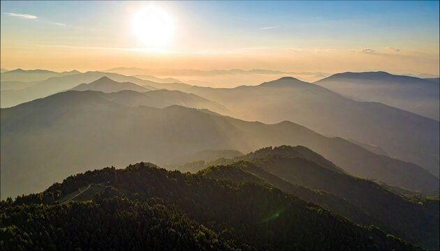 Aerial view of a mountain range at sunset, with layers of hills and a hazy atmosphere, illuminated by the sun's golden light. - Powered by Adobe