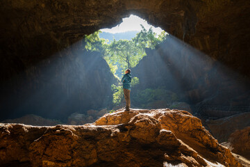 Man With Arms Outstretched Embracing Sunbeams in Giant Tiankeng Sinkhole Cave in Guangxi China
