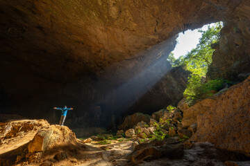 Man With Arms Outstretched Embracing Sunbeams in Giant Tiankeng Sinkhole Cave in Guangxi China