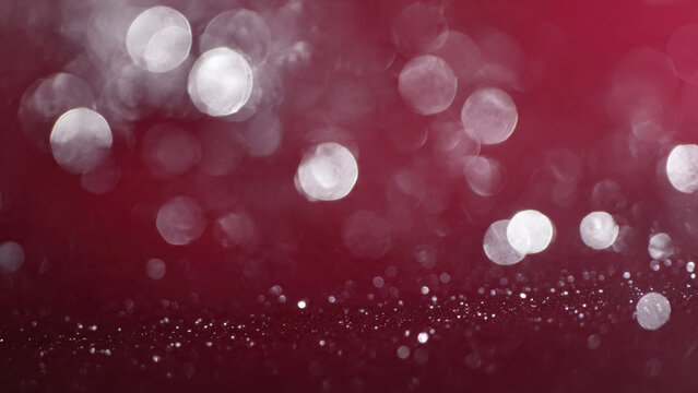 A festive abstract background featuring shimmering white bokeh circles floating above a sparkling glitter surface on a rich red backdrop.