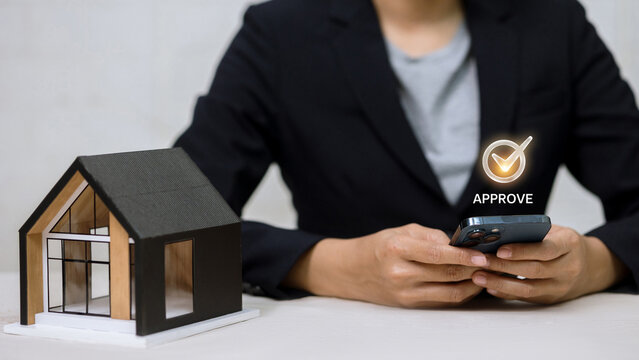 Businesswoman holding smartphone with approve icon and house model. Mortgage loan concept.
