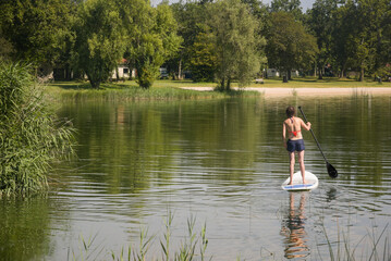 Une femme sur un paddle sur un lac. Balade en paddle l'&eacute;t&eacute;. Sport aquatique. Loisir sur un lac en &eacute;t&eacute;. Vacances vers un &eacute;tang