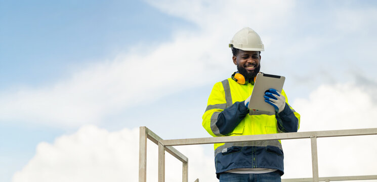 African Engineer man working on tablet computer in field with wind turbines background, Windmill. environmental renewable clean energy. Wind power generation. Windmill engineer inspection progress