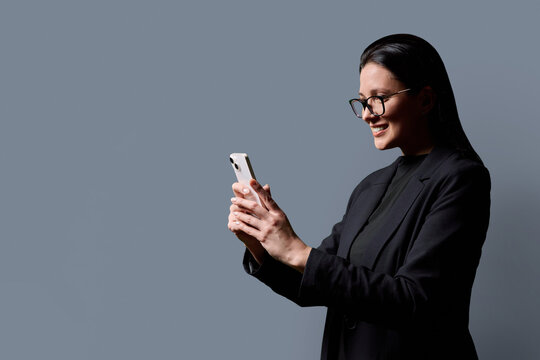 Profile portrait of successful middle-aged businesswoman with smartphone on grey background - Powered by Adobe
