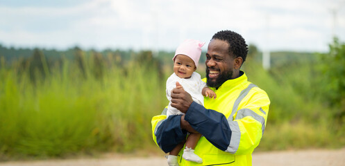 Fototapeta premium Portrait African engineering man with baby standing in field with wind turbines in the background, Windmill. environmental renewable clean energy. Wind power generation. Nature Outdoor activitie