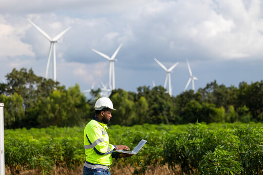 laptop computer. African Engineer man working in field with wind turbines background, Windmill. environmental renewable clean energy. Wind power generation. Windmill engineer inspection progress