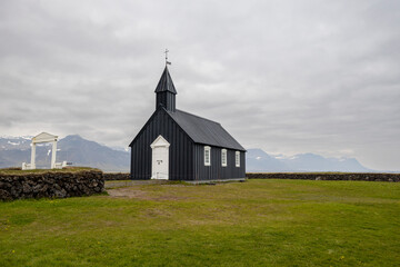 The black wooden church of B&uacute;&eth;akirkja with white gate and windows and stone fence, Snaefellsnes peninsula, Iceland
