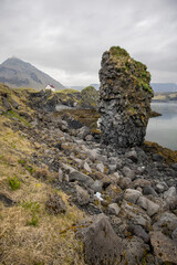 basalt sea stack at the entrance of Arnarstapi port with the iconic white house and Mt Stapafell in the background, Snaefellsnes Peninsula, West Iceland