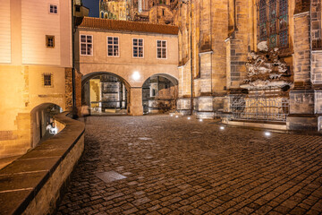 Obraz premium The covered bridge next to Saint Vitus Cathedral illuminates the cobblestone path in Prague Castle at night, showcasing the historic architecture under soft street lighting.