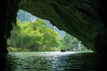 Silhouette of Boat Exiting Cave Through Arch Opening to Lush Karst River Landscape in Guangxi China