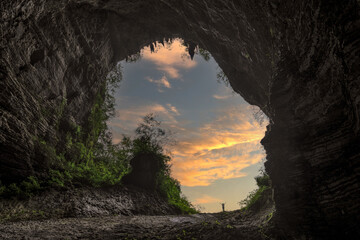 Silhouette of Person With Arms Raised at Cave Entrance During Dramatic Sunset