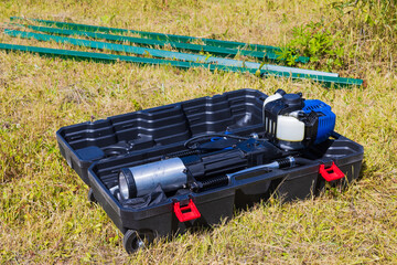 Hand-held petrol pile driver in a case and metal poles lie on the lawn. Concept of do-it-yourself...