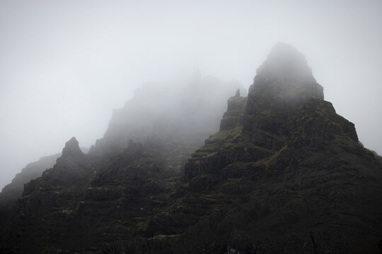 View of jagged, dark, imposing mountains shrouded in a mysterious, heavy fog, their peaks barely visible in the monochrome landscape, Jokulsarlon, Sveitarfelagid Hornafjordur, Iceland.