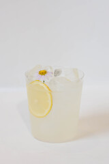 A refreshing lemonade with ice and a lemon slice, garnished with flower, in a glass