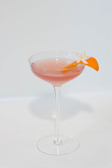 A refreshing cocktail garnished with an orange slice and delicate flower. The drink is a light pink color, perfect for summer or a special occasion.