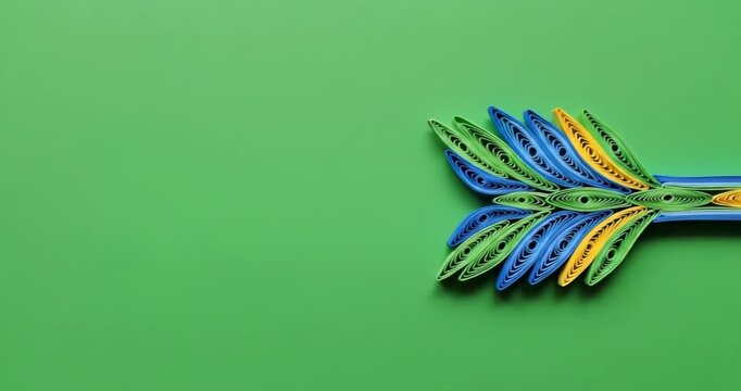 Quilled paper arrow craft in blue, green, and yellow colors against a solid bright green background