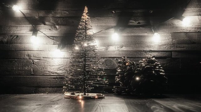 A small, decorated Christmas tree stands on a wooden surface, illuminated by warm string lights against a rustic wooden wall.