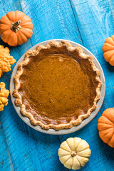 Top view of classic pumpkin pie with spices and ingredients arranged around