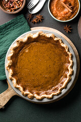 Top view of classic pumpkin pie with spices and ingredients arranged around