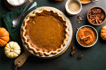 Top view of classic pumpkin pie with spices and ingredients arranged around