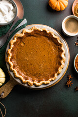 Top view of classic pumpkin pie with spices and ingredients arranged around