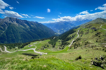 Panoramic view into Passeier Valley (germ. Passeiertal) from Jaufenpass in South Tyrol, Italy with winding mountain road, green pastures and forested slopes under a blue sky © A. Emson