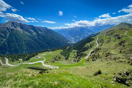 Panoramic view into Passeier Valley (germ. Passeiertal) from Jaufenpass in South Tyrol, Italy with winding mountain road, green pastures and forested slopes under a blue sky