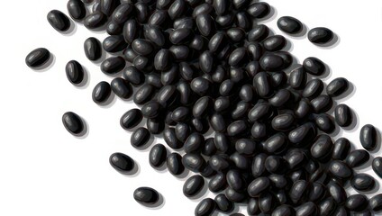 A pile of raw black turtle beans scattered on a clean white background from a top down view.