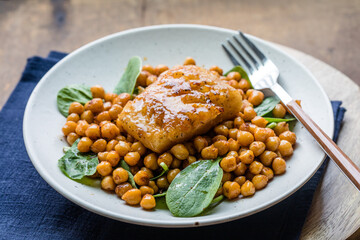Pan-seared cod served with chickpeas and fresh spinach on a white plate