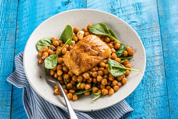 Pan-seared cod served with chickpeas and fresh spinach on a white plate