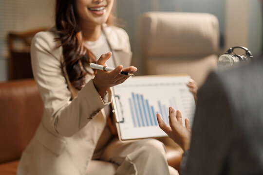 Business woman presenting financial data chart during a podcast interview, sharing insights with a microphone nearby