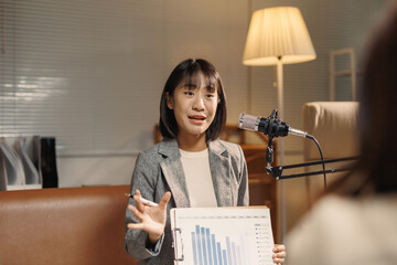 Asian businesswoman hosting a business podcast, presenting a data chart to an unseen guest, discussing financial growth and strategy