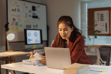 Concentrated businesswoman in an office working late hours with laptop, documents, and charts. Concept of overtime and dedication