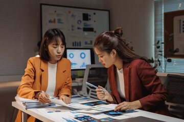 Young Asian businesswomen collaborating on financial data analysis using charts and graphs in a contemporary office setting