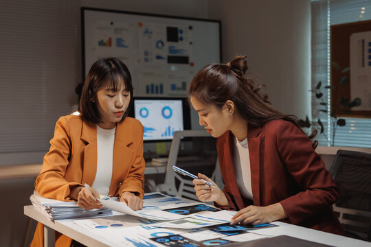 Young Asian businesswomen collaborating on financial data analysis using charts and graphs in a contemporary office setting