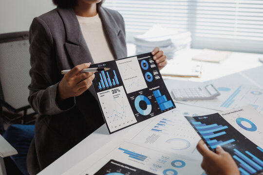 Businesswoman holding a report, pointing at charts and graphs while discussing financial data with a colleague in an office