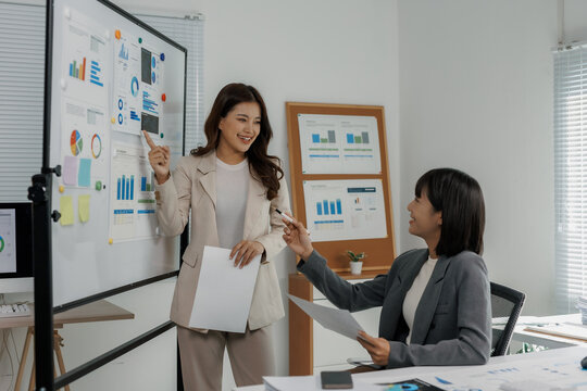 Asian businesswomen presenting financial charts during an office meeting, analyzing data for planning and teamwork