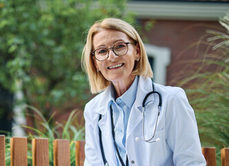 Portrait of a mature older female woman doctor or nurse and  health care worker using a smartphone mobile phone  in front of hospital or clinic outside