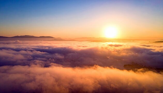 An aerial view of a sunrise above a sea of clouds, with mountains in the distance. The sun is bright and the sky is a gradient of colors.