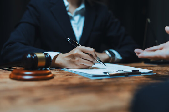 Legal professional in business suit signing a contract or agreement document on a clipboard during a consultation about judicial matters